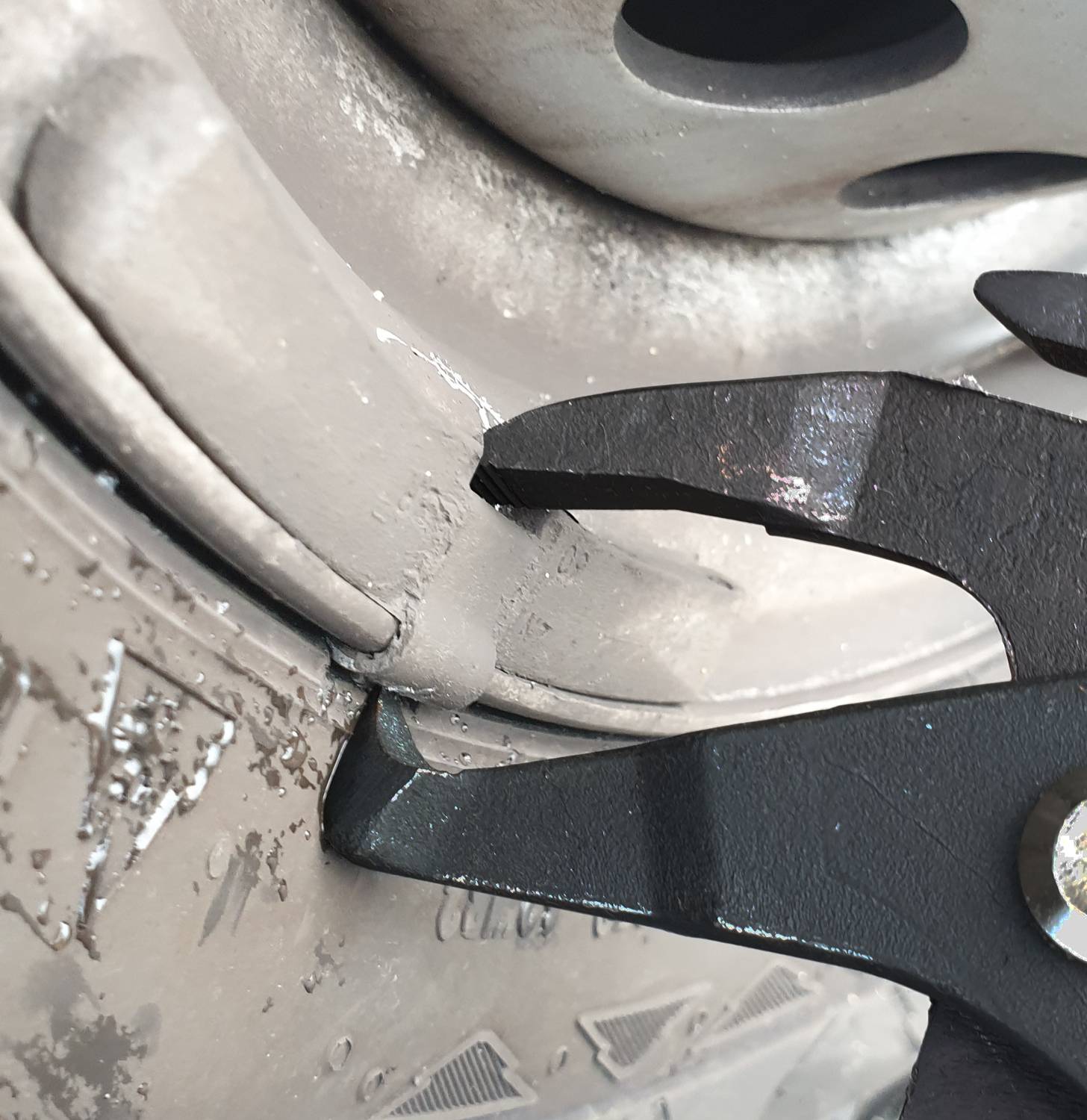 Nahaufnahme eines Reifenwechselwerkszeugs, das in eine Felge eingreift, vermutlich während eines Reifenwechsels oder einer Reparatur.