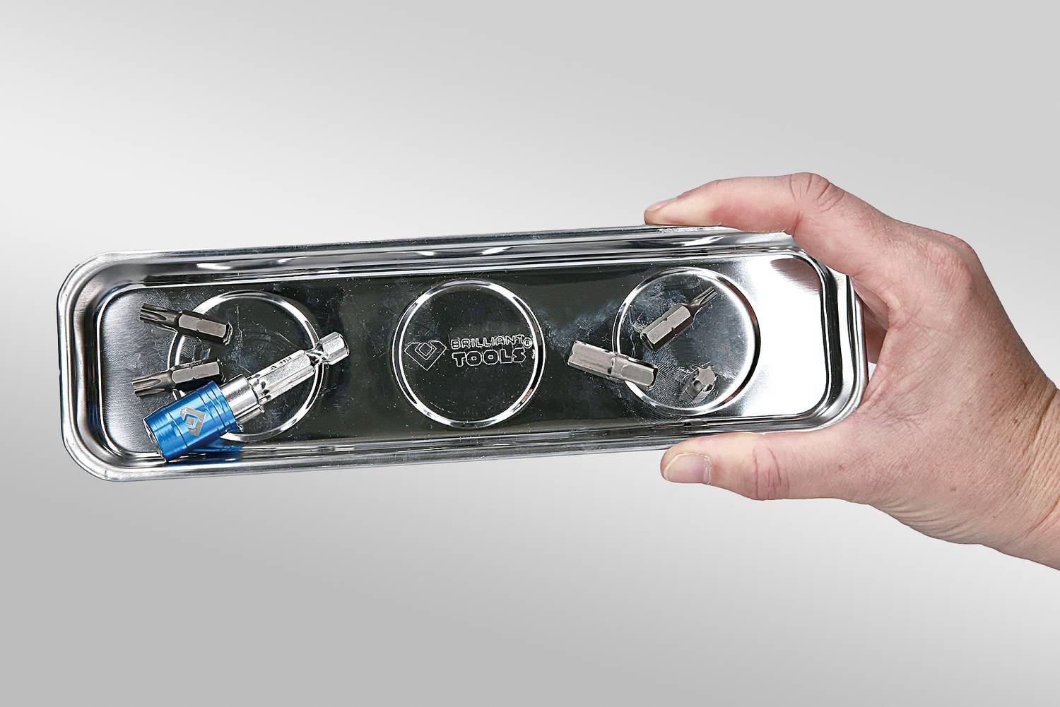 Eine Hand hält ein ovales Metalltablett mit Schrauben und einer blauen Sicherungsmutter, die durch Magnetkraft fixiert sind.