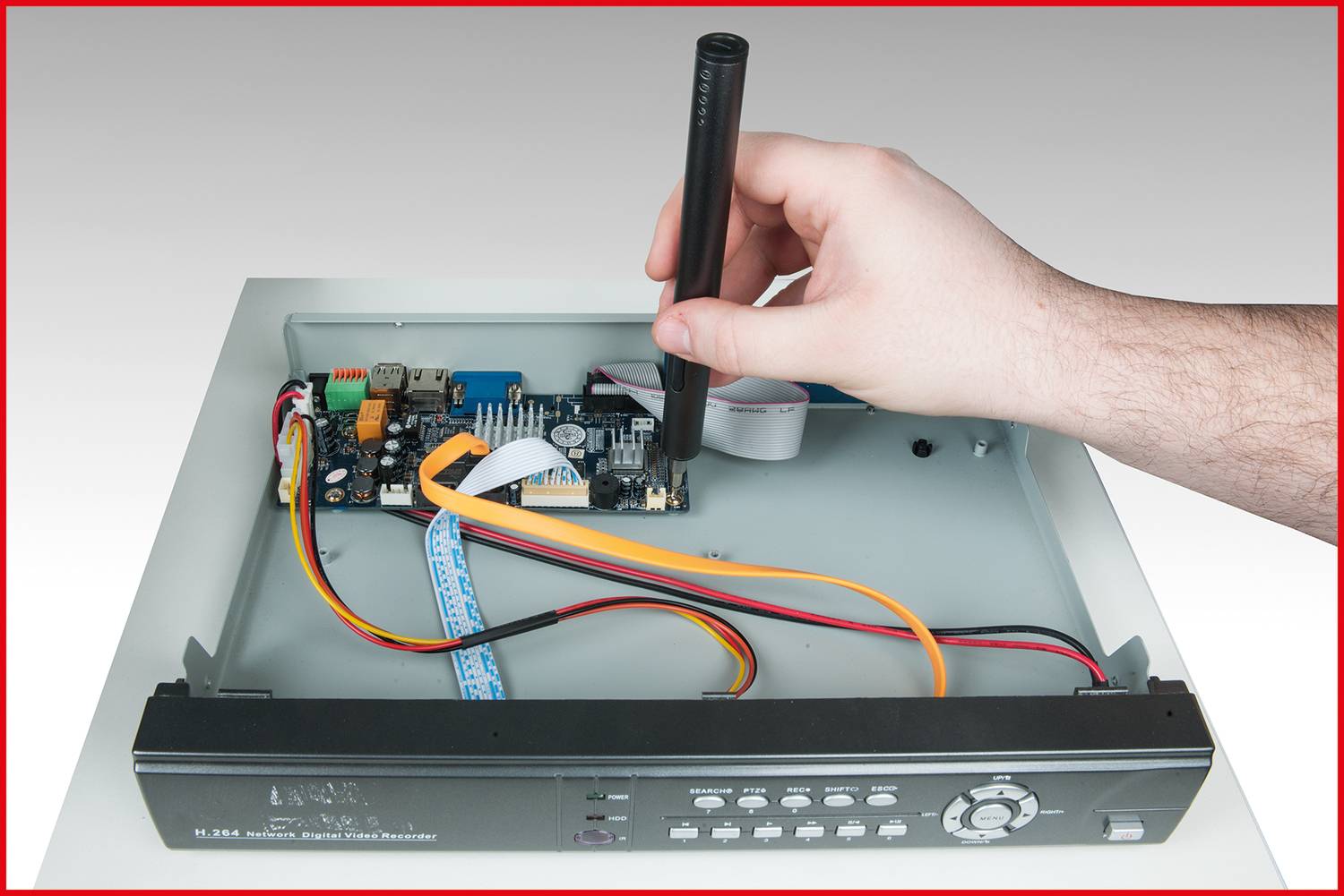 Hand verwendet Werkzeug zum Arbeiten an offener Elektronikplatine in Gehäuse mit sichtbaren Kabeln und Platinenkomponenten.