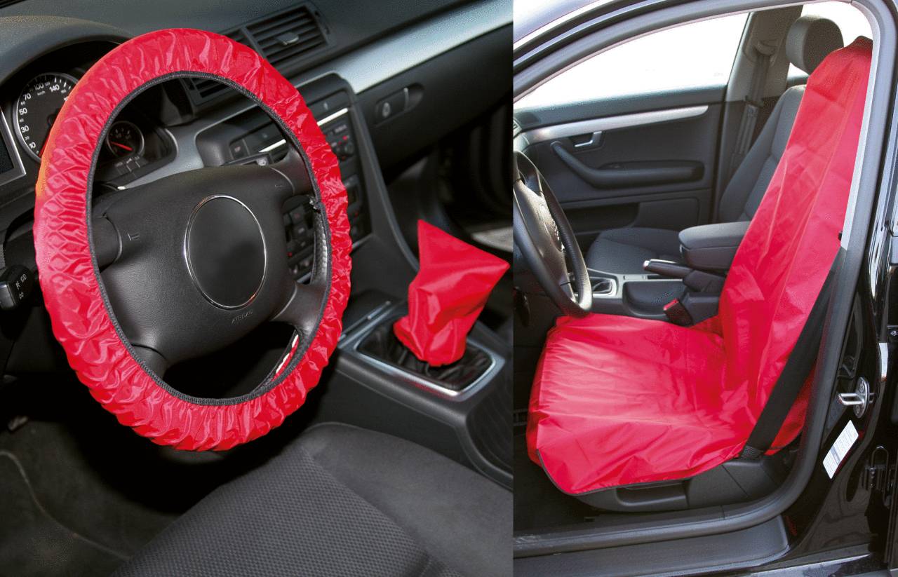 Lenkrad, Schalthebel und Autositz eines Fahrzeugs sind mit roten Schonbezügen für Schutz abgedeckt. Beifahrertür offen.