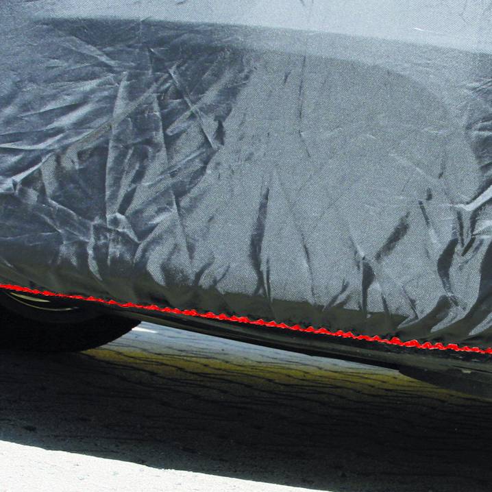 Ein dunkles Auto ist teilweise unter einer Abdeckung vor der Sonne geschützt. Darunter sind Reifen sichtbar, die auf Asphalt stehen.