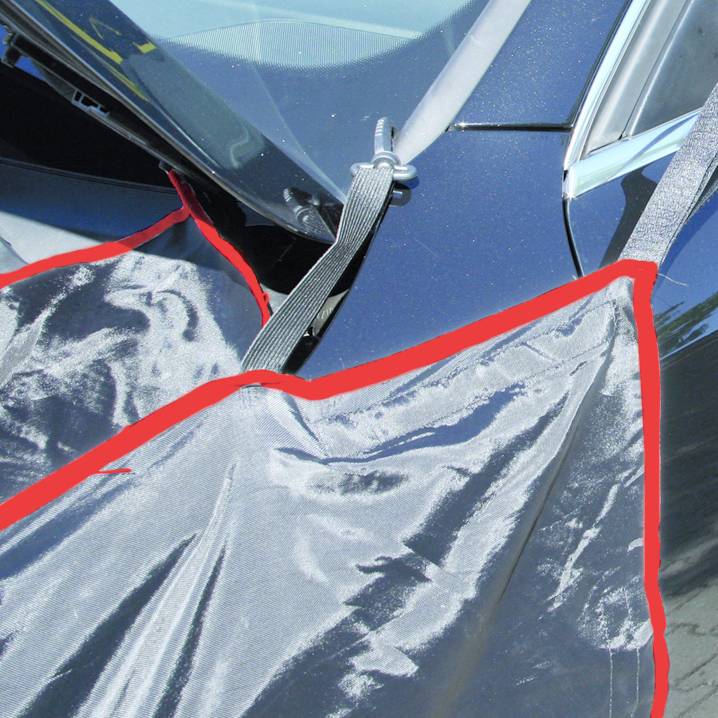 Auto mit Abdeckplane an der Windschutzscheibe befestigt. Die Plane hat rote Kanten und schützt vor Witterungseinflüssen.