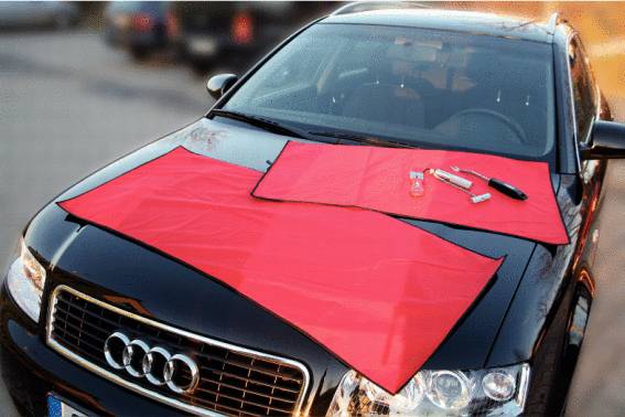 Schwarzes Auto mit roten Tüchern auf der Motorhaube; daneben liegen Werkzeuge.