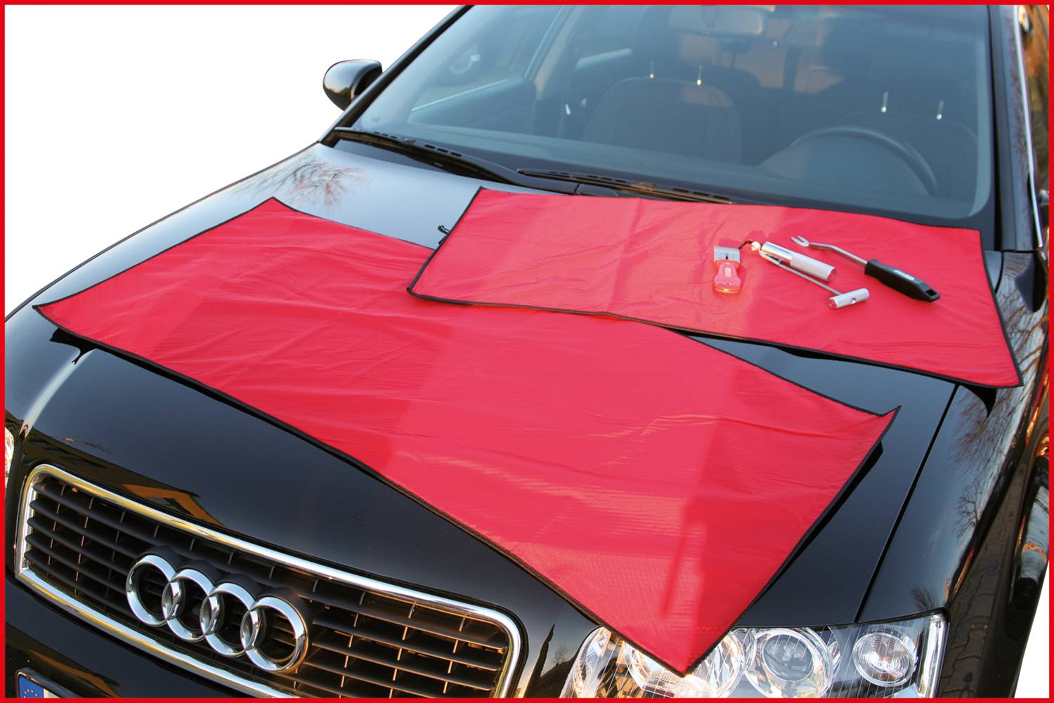 Roter Schutzbezug auf schwarzer Autokarosserie, mit einigen Werkzeugen darauf platziert.