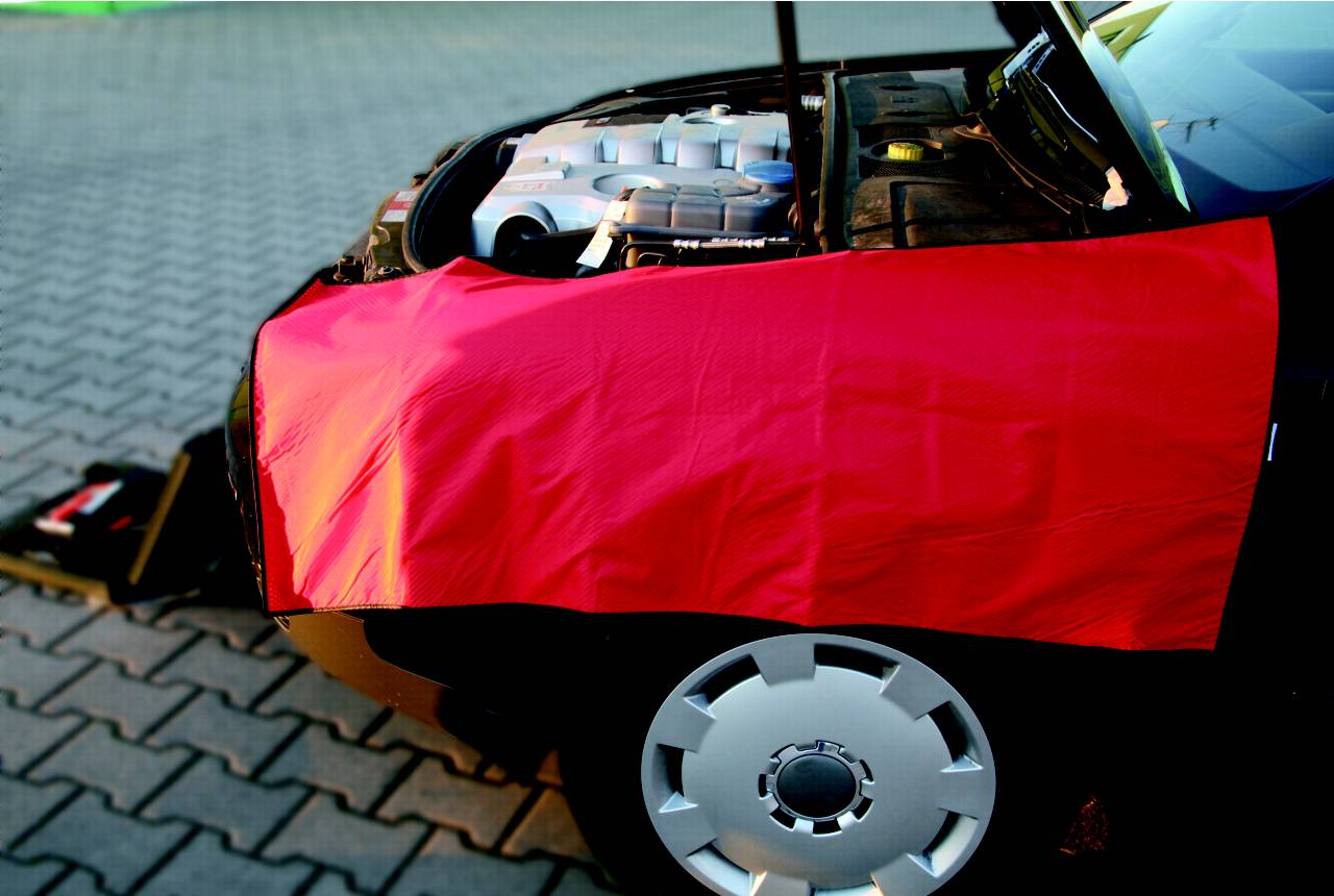 Auto mit geöffnetem Motorhaube, rote Schutzdecke bedeckt den vorderen Kotflügel, auf einem gepflasterten Boden geparkt.