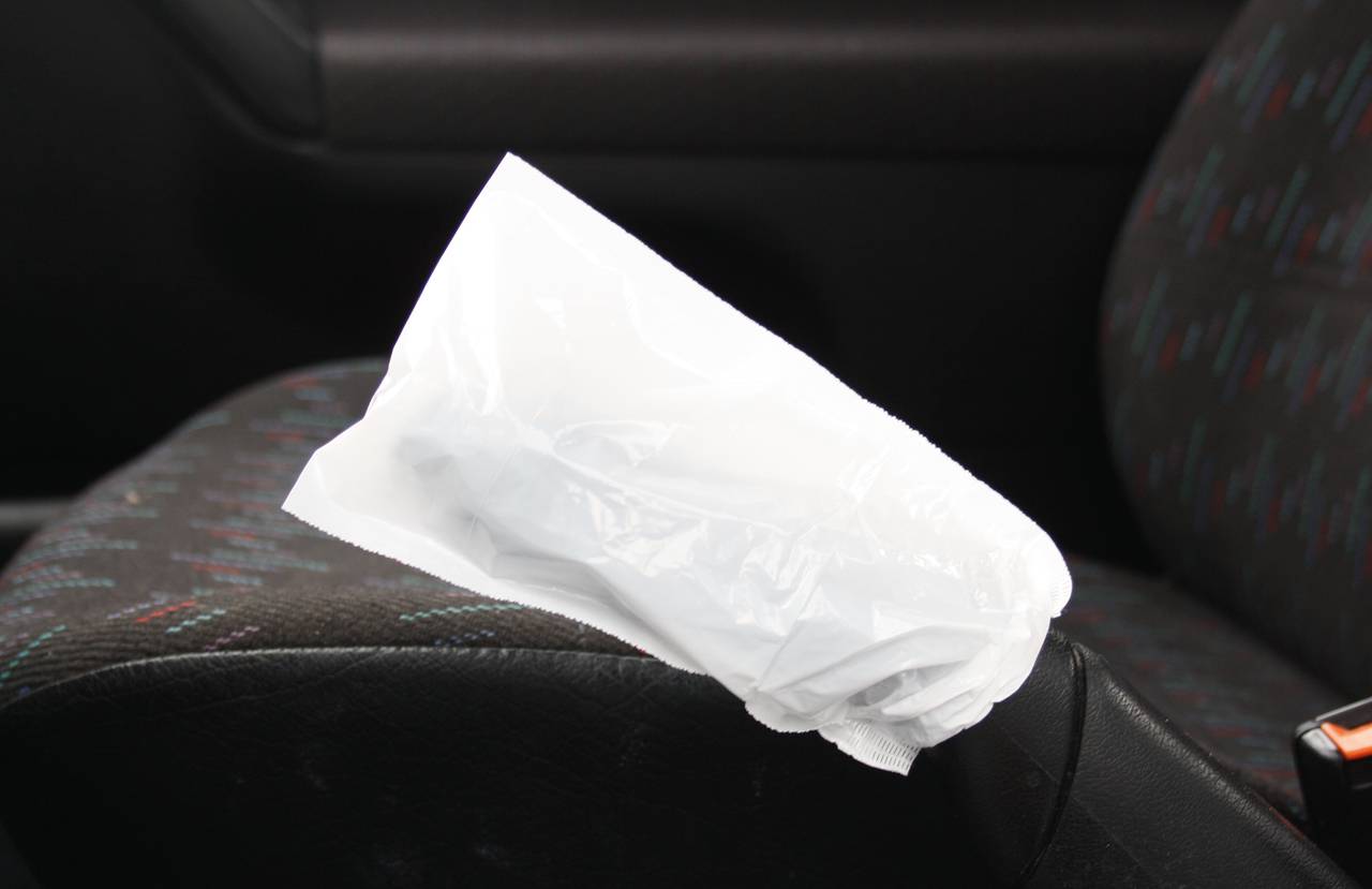 Eine geschlossene weiße Plastiktüte liegt auf dem Sitz eines Autos. Sie verdeckt teilweise die Sitzoberfläche.