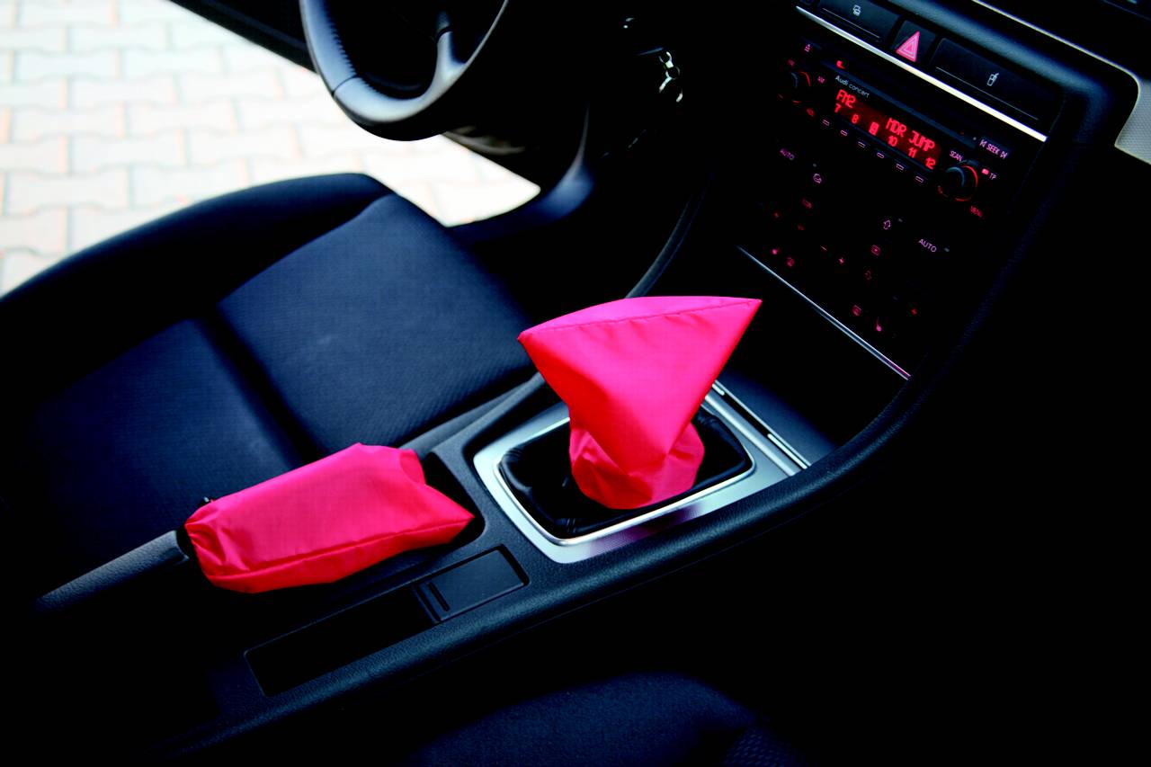 Ein Autoinnenraum mit schwarzer Ausstattung. Der Schalthebel und die Handbremse sind mit leuchtend pinken Manschetten überzogen.