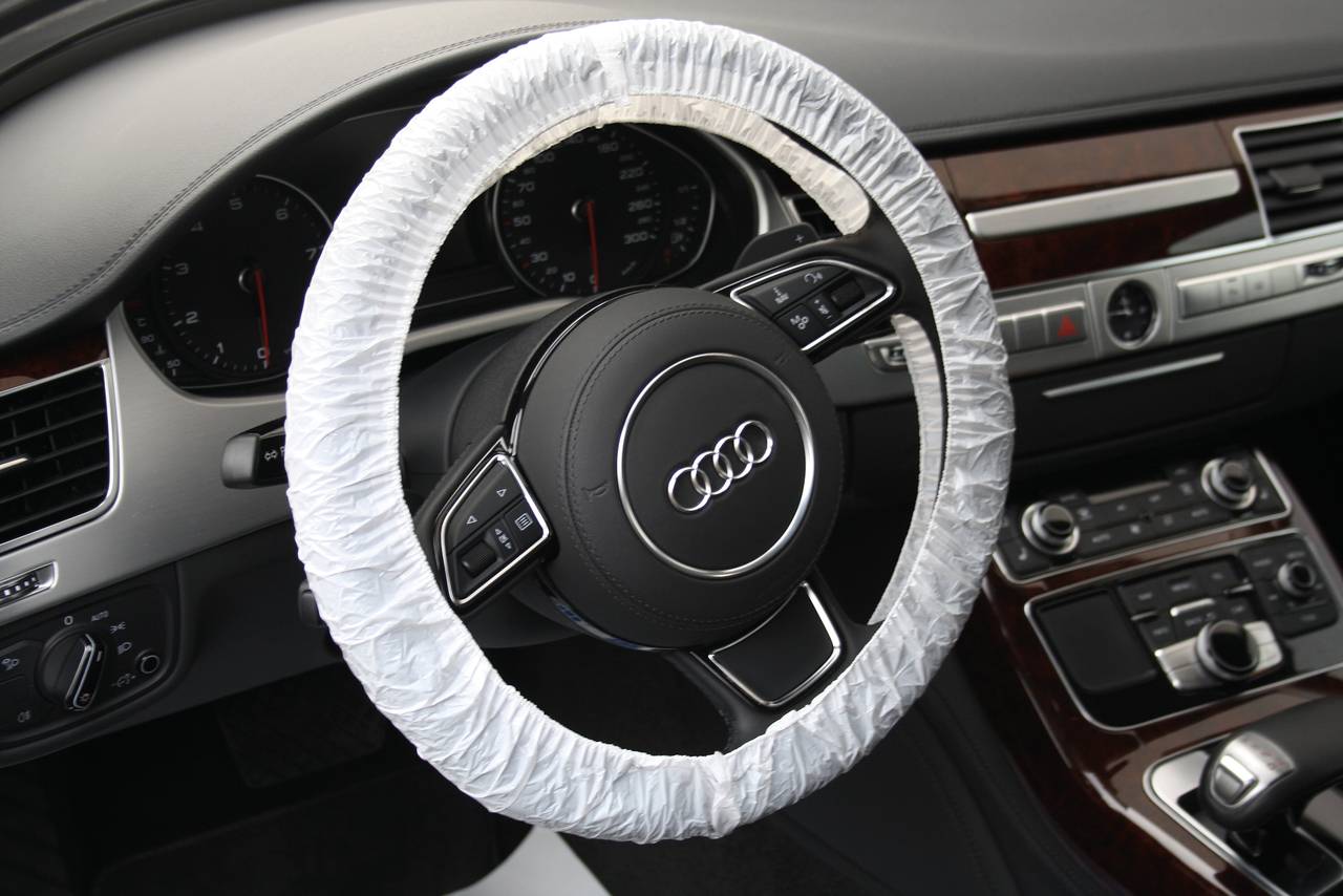 Lenkrad eines Audi mit Schutzabdeckung. Bedienknöpfe am Lenkrad sichtbar, Innenraum im Hintergrund.