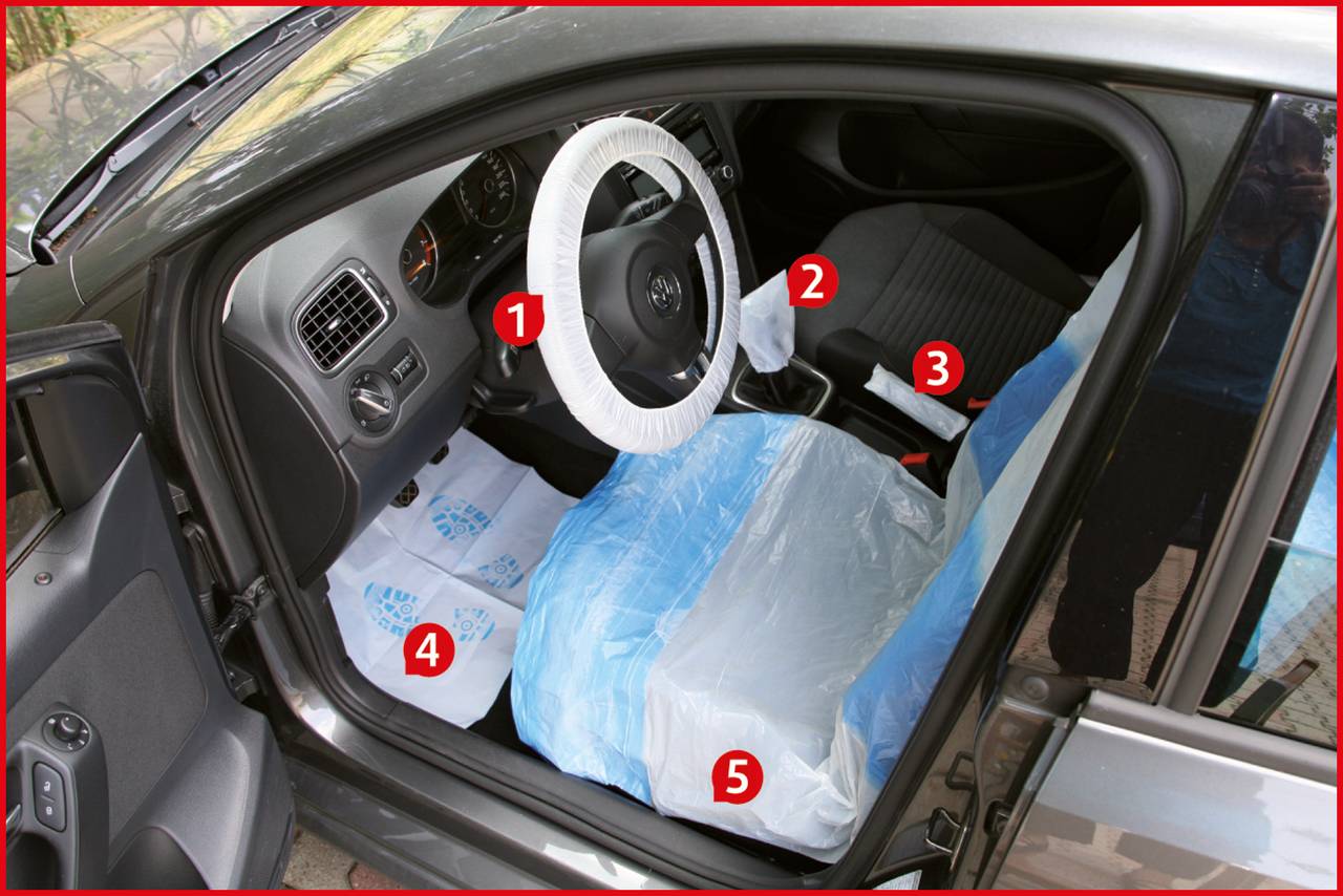 Innenraum eines Autos mit Abdeckungen auf Lenkrad, Sitz und Boden, wahrscheinlich als Schutz beim Transport oder bei Wartungsarbeiten.