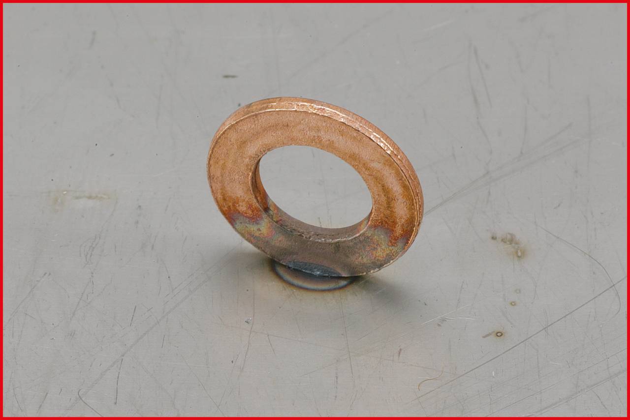 Eine bronzefarbene Metallunterlegscheibe liegt auf einer grau strukturierten Oberfläche.