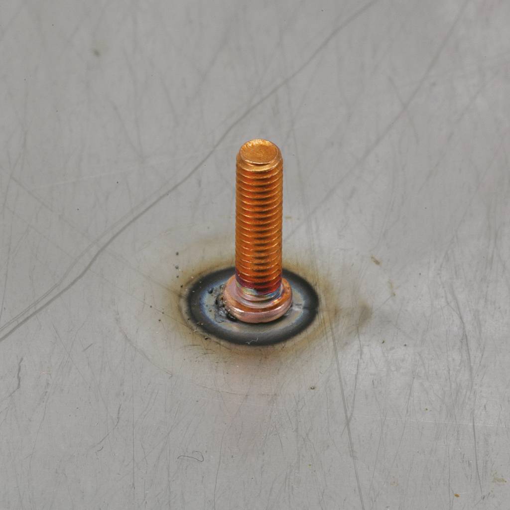 Ein Bolzen ist auf einer Metalloberfläche mit einem Schweißpunkt befestigt. Der Bolzen ist orange und kontrastiert mit dem grauen Metall.