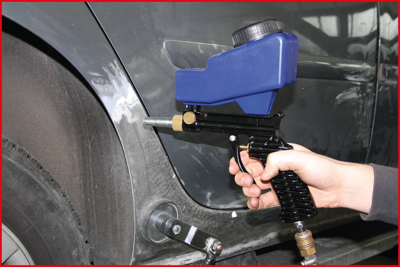 Eine Person hält eine Spritzpistole und arbeitet an der Reparatur eines Autos. Die Fahrzeugseite zeigt Schleifspuren.