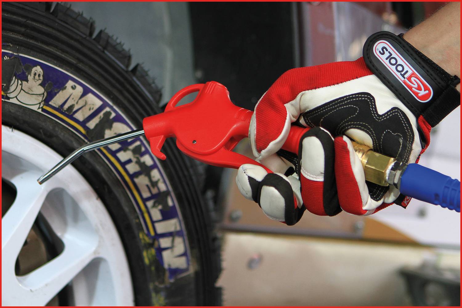 Eine Hand in einem rot-weißen Handschuh hält ein Druckluftgerät nahe einem Autoreifen mit 'Michelin'-Schriftzug.