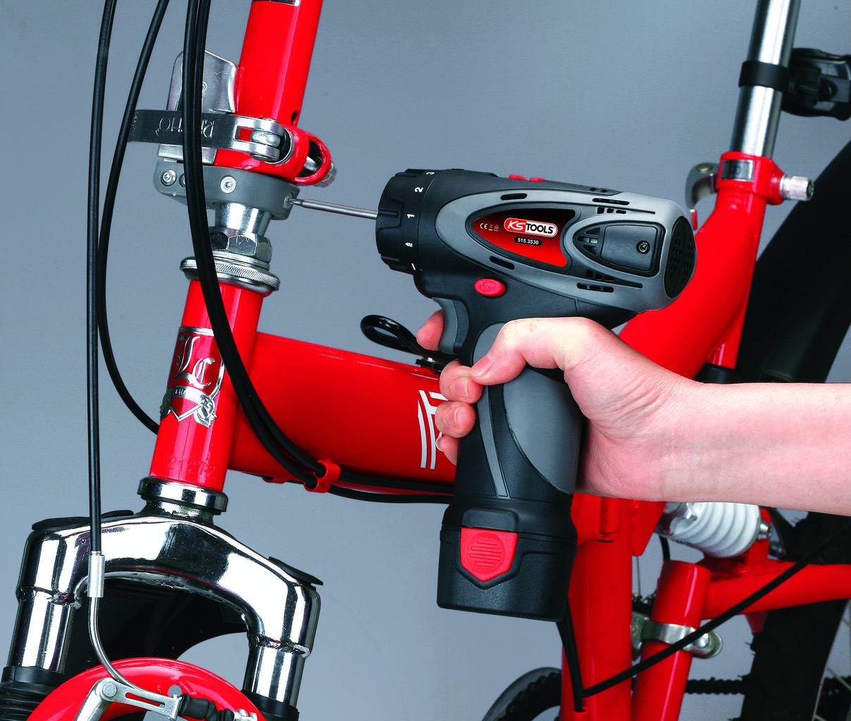 Eine Person befestigt eine Schraube an einem roten Fahrradrahmen mit einem Akkuschrauber.