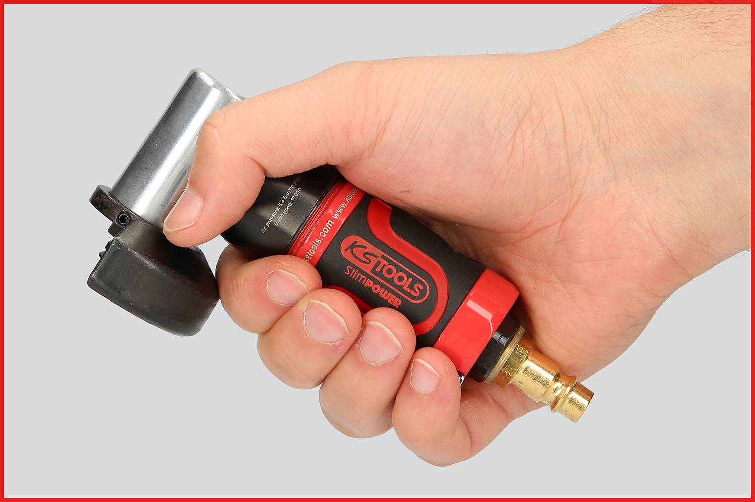 Eine Hand hält ein rotes und schwarzes Werkzeug mit Metallaufsatz, das eine Verbindung für Druckluft zeigt.