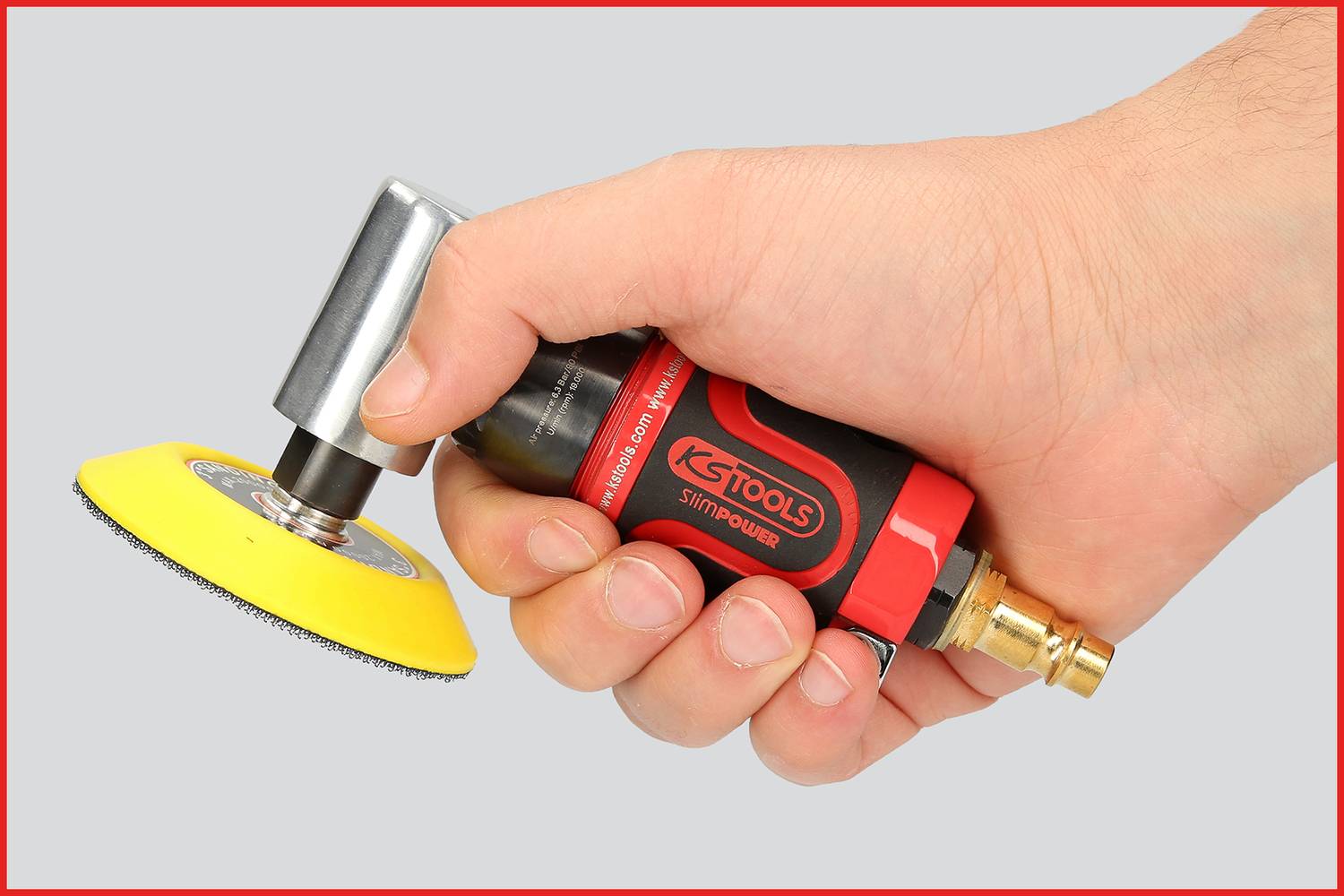 Eine Hand hält ein rotes und schwarzes Druckluftwerkzeug mit gelbem Polieraufsatz. Das Werkzeug befindet sich in Bereitschaft.