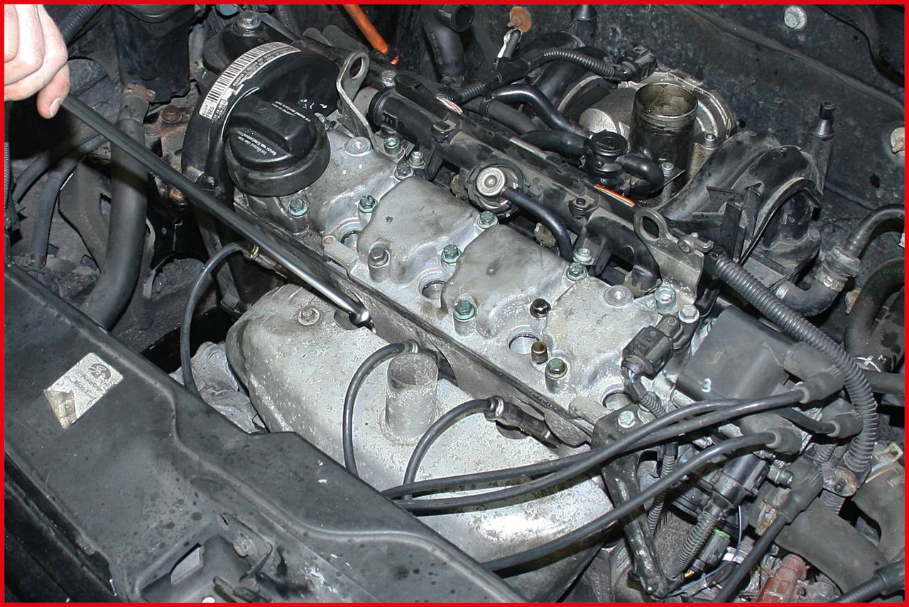 Auto-Motor in Nahaufnahme während einer Wartung. Eine Hand arbeitet mit einem Schraubenschlüssel an den Verbindungen der Zylinderkopfabdeckung.