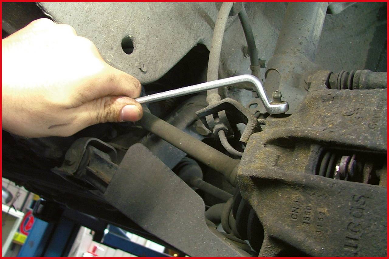 Ein Mechaniker zieht mit einem Inbusschlüssel eine Schraube an der Bremsanlage eines Autos an.