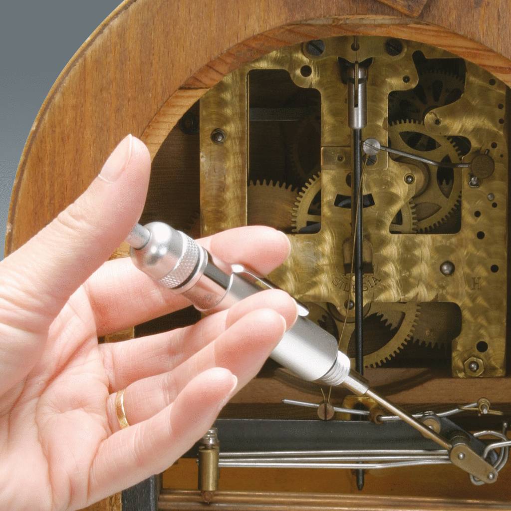 Eine Hand bedient ein präzises Messinstrument vor einem komplexen Uhrwerk, das Zahnräder und Mechaniken zeigt.