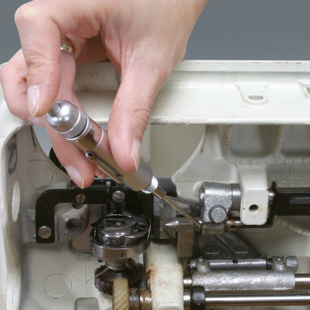 Eine Hand repariert das Innenleben einer Nähmaschine mit einem Schraubendreher und einer kleinen Bürste, zeigt Präzision und Mechanikarbeit.