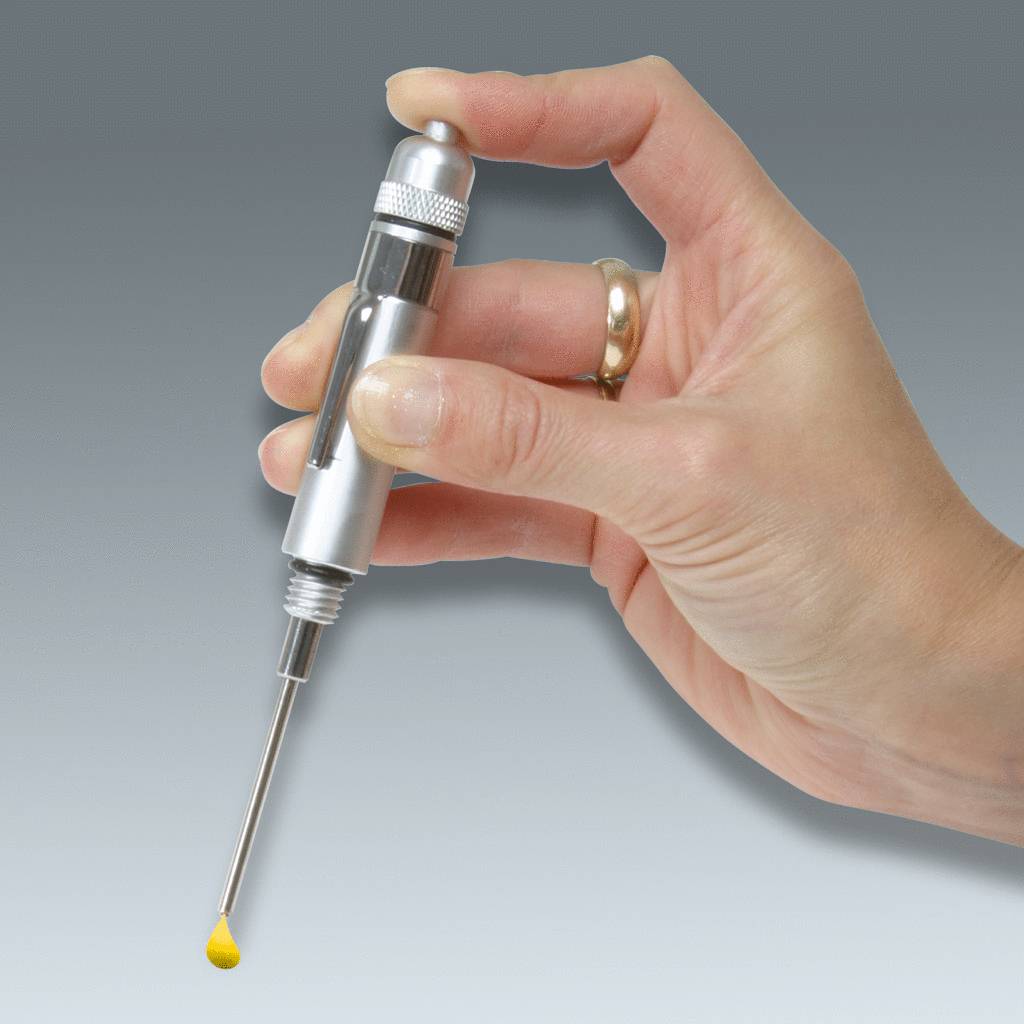 Eine Hand hält eine silberne Pipette, die eine gelbe Flüssigkeitstropfen am Ende hat. Der Hintergrund ist grau.