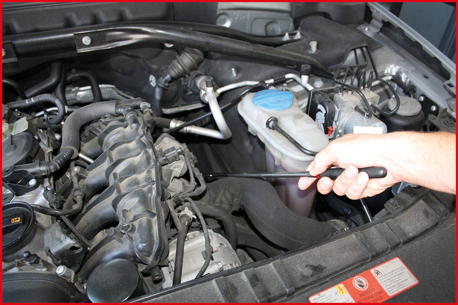 Eine Hand zieht den Ölmessstab aus dem Automotor, um den Ölstand zu prüfen. Der Motorraum zeigt verschiedene Autoteile.