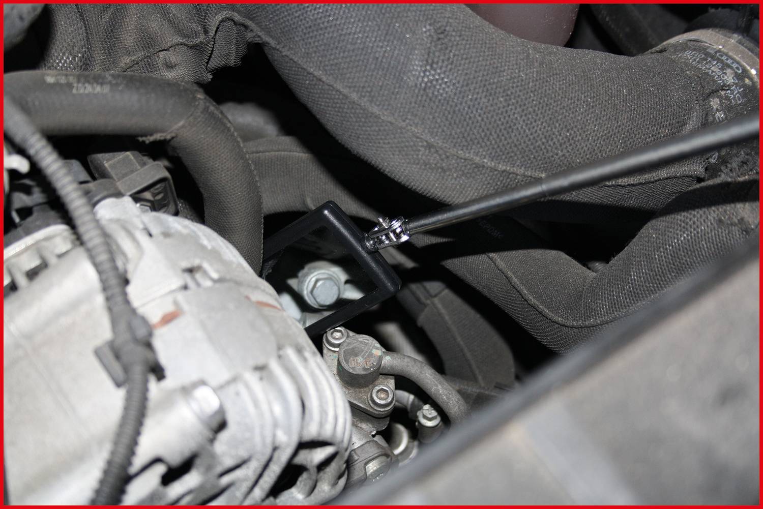 Nahaufnahme eines Motorraums mit einem Metallbolzen, der von einem schwarzen Kabel umgeben ist. Ein Teil des Motors ist sichtbar im Hintergrund.