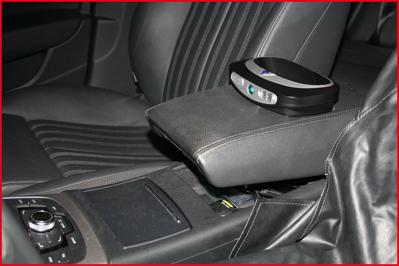 Ein kleines, schwarzes Gerät mit digitaler Anzeige auf der Mittelarmlehne eines Autos, vermutlich zur Speicherung von Gegenständen.