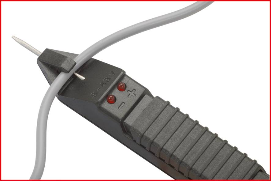 Ein Spannungsprüfer liegt neben einem grauen Kabel. Zwei rote Lichter sind sichtbar. Der Prüfer zeigt '12-48V'.