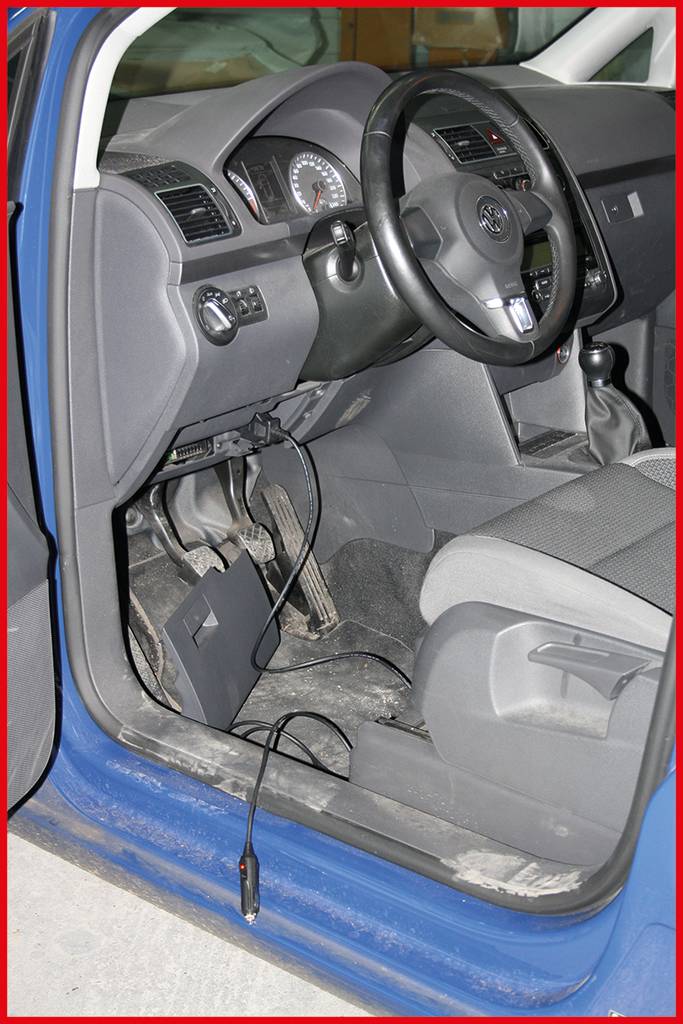 Ein offenes Auto mit blauem Türrahmen zeigt den Innenraum und die Pedale. Ein Kabel ist am Boden sichtbar, das aus dem Armaturenbrett kommt.