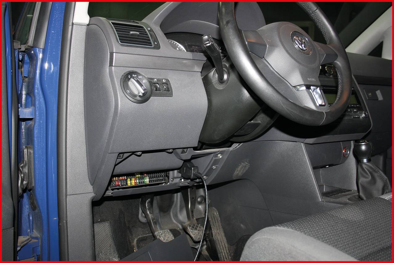Innenraum eines Autos, Fokus auf Armaturenbrett und Lenkrad. Ein technisches Gerät ist unterhalb des Lenkrads installiert.