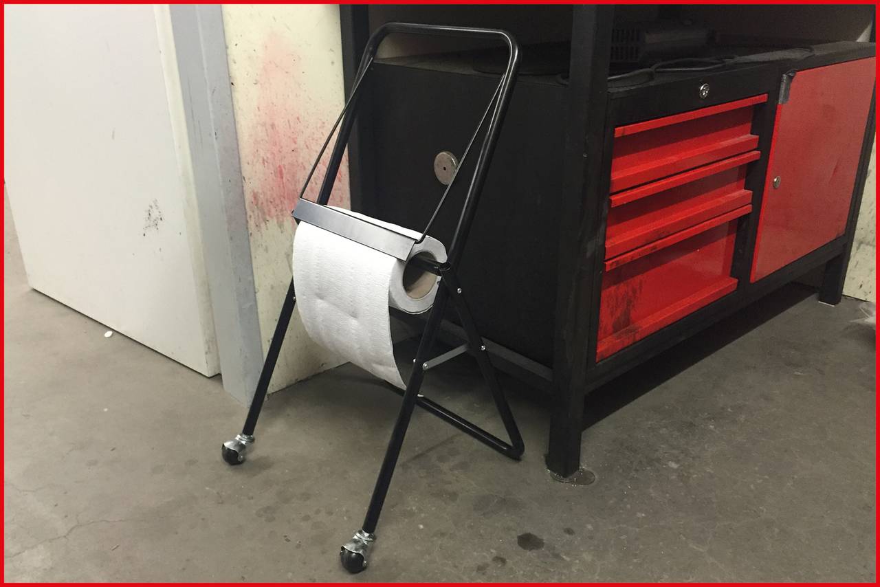 Ein Toilettenpapierhalter auf Rollen steht vor einem schwarzen Werkzeugschrank mit roten Schubladen in einer Werkstattumgebung.
