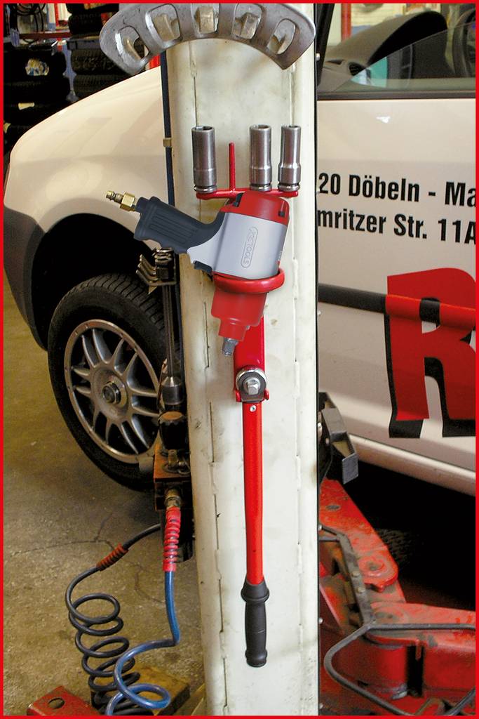 Ein Radmutternschlüssel mit Druckluftantrieb hängt an einem Werkstattständer. Im Hintergrund ist ein weißes Auto sichtbar.