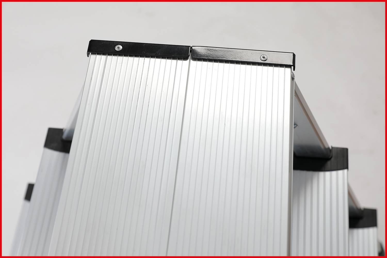 Silberne Aluminiumleiter, frontal fotografiert. Die Streben sind gerippt für besseren Halt. Oberer Teil der Leiter vor neutralem Hintergrund.