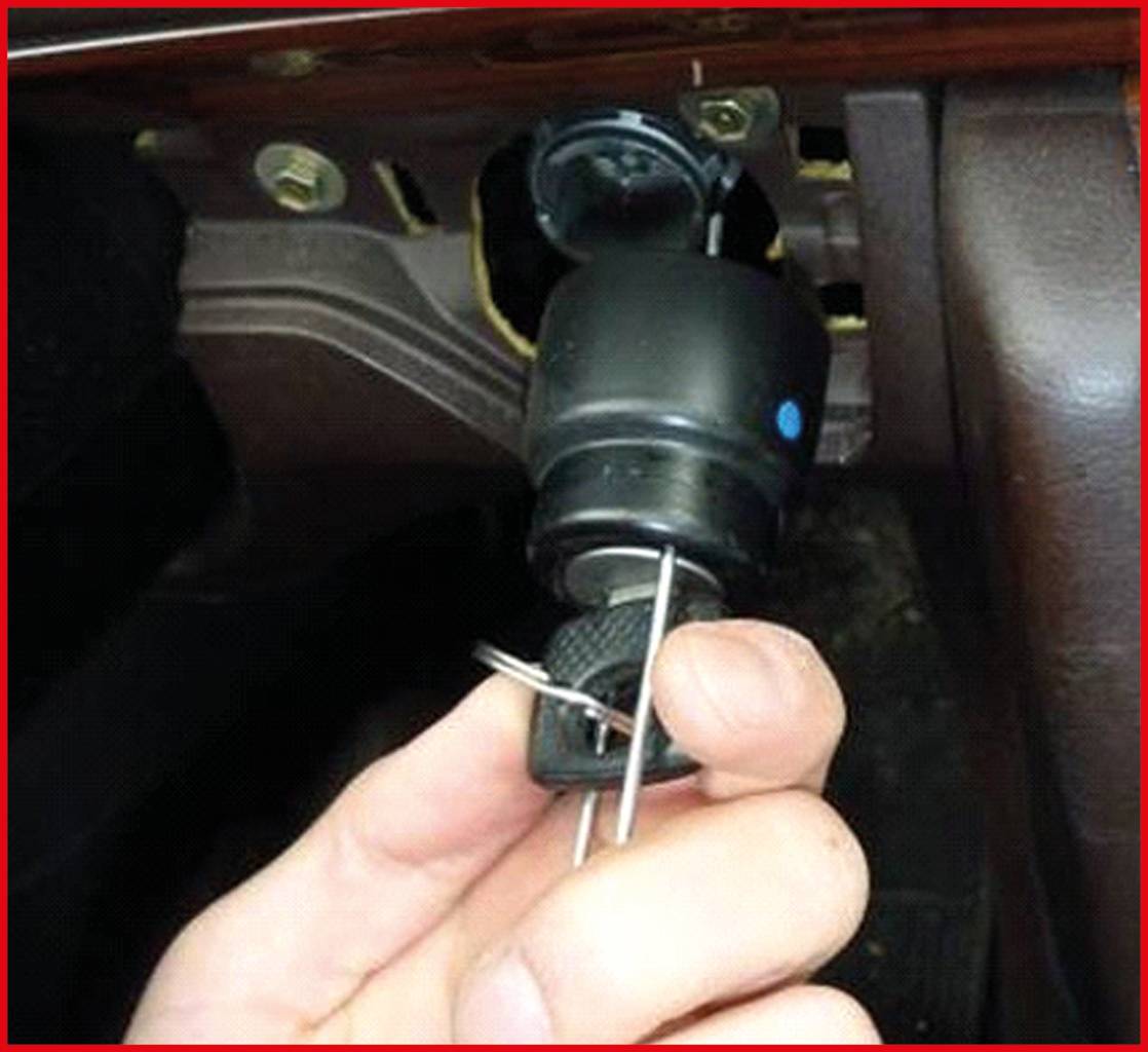 Eine Hand hält ein Auto-Zündschloss mit einem Werkzeug. Das Zündschloss ist ausgebaut und zeigt den mechanischen Aufbau.