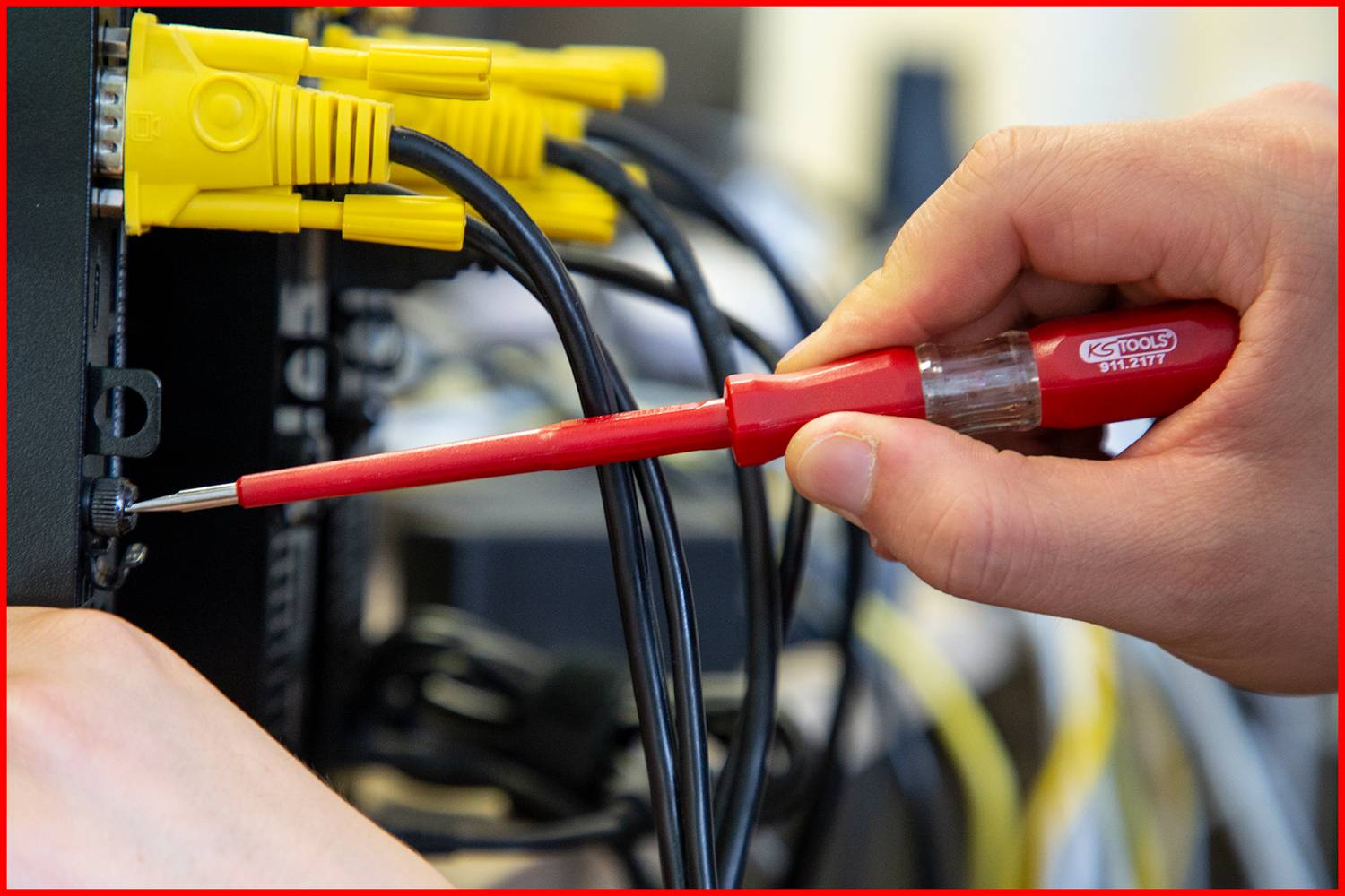 Eine Hand hält einen roten Schraubenzieher und zieht eine Schraube an einem Netzwerkgerät fest. Gelbe Kabel sind oben verbunden.