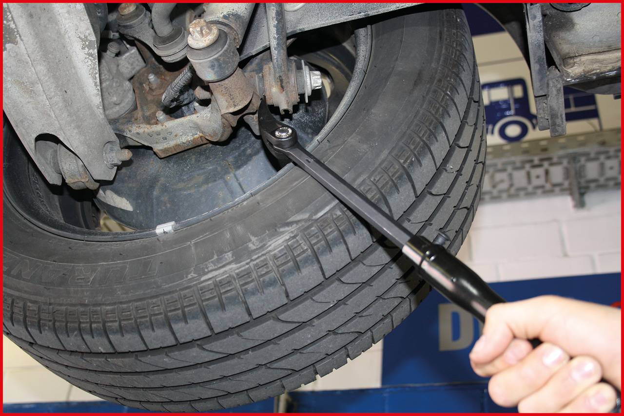 Eine Hand zieht mit einem Steckschlüssel die Schrauben an einem Autoreifen an. Der Reifen ist angehoben und Teil eines Fahrgestells.