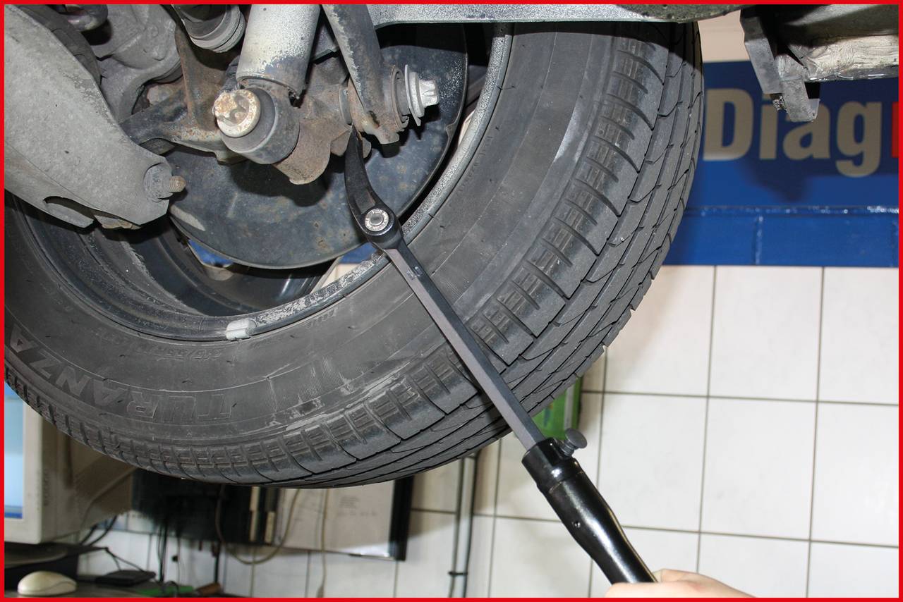 Nahaufnahme eines Autoreifens in einer Werkstatt, der von einem Mechaniker mit einem Drehmomentschlüssel bearbeitet wird.