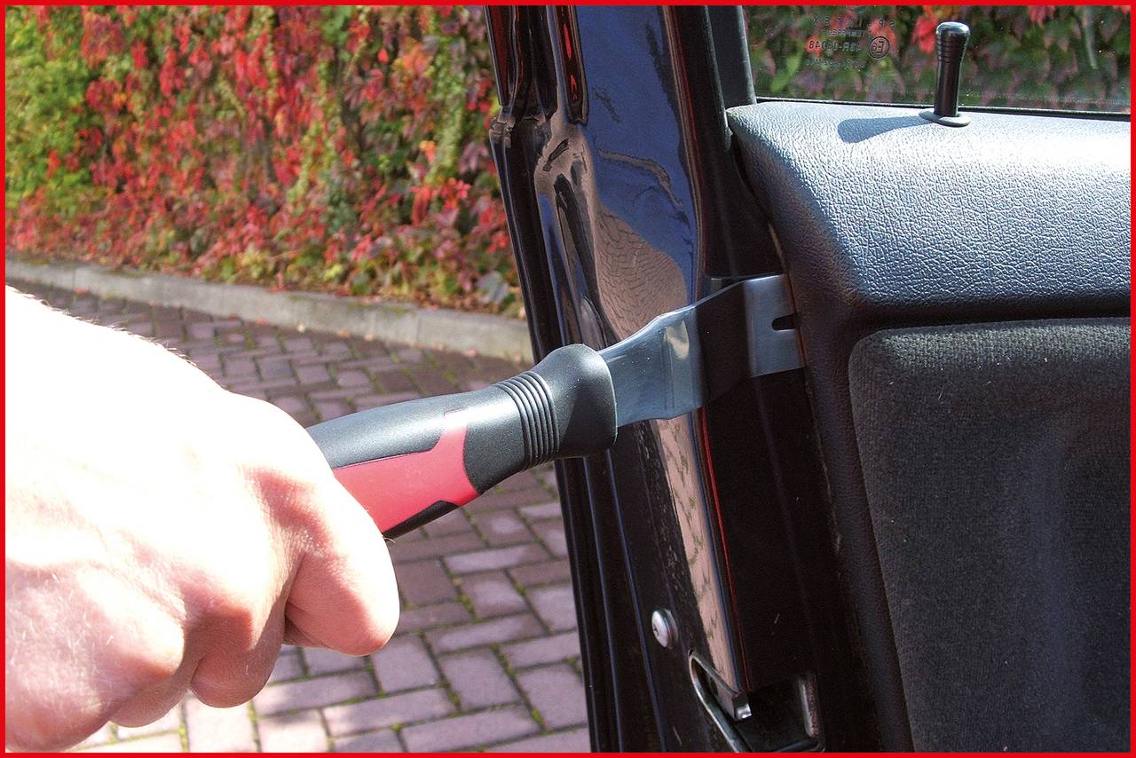 Eine Hand hält einen Schraubendreher, der zwischen Autotür und Rahmen eingeführt wird, was auf einen möglichen Einbruchsversuch hinweist.