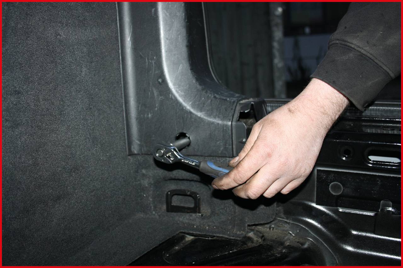 Eine Person zieht mit einem Schraubenschlüssel eine Schraube in einem Autokofferraum fest.