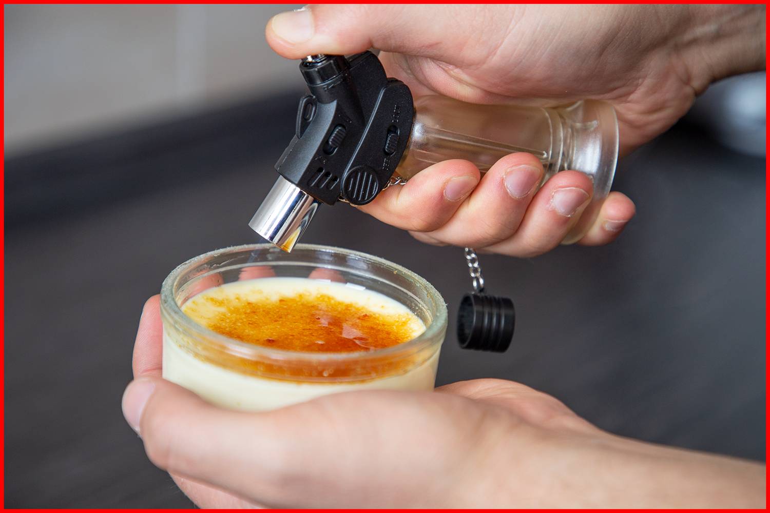 Eine Hand hält einen kleinen Flambierbrenner über eine Crème brûlée, um die Zuckeroberfläche zu karamelisieren.