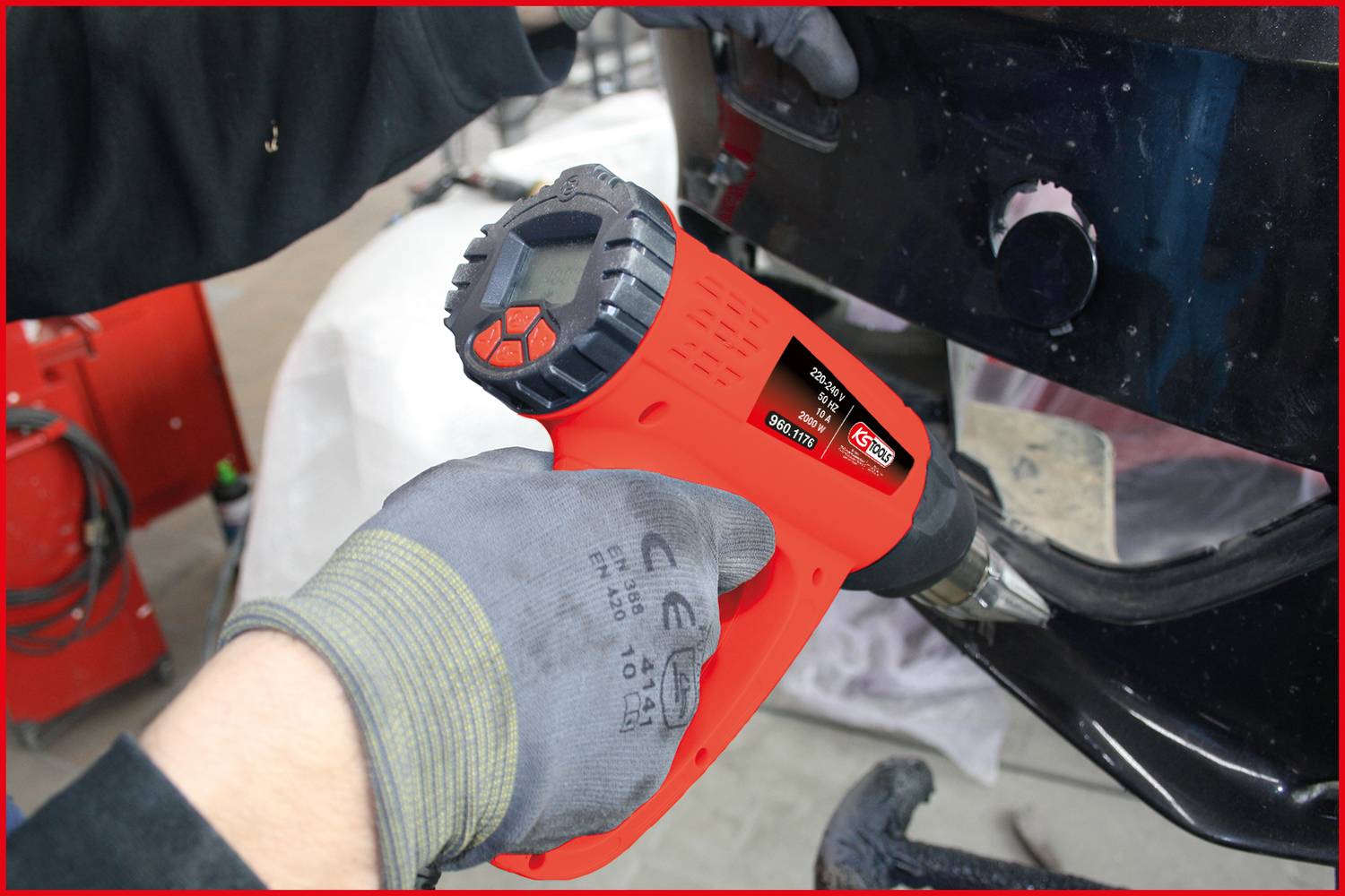 Person verwendet eine rot-schwarze Heißluftpistole, um ein Automaterial zu bearbeiten. Werkzeug hat Display und Bedienelemente.