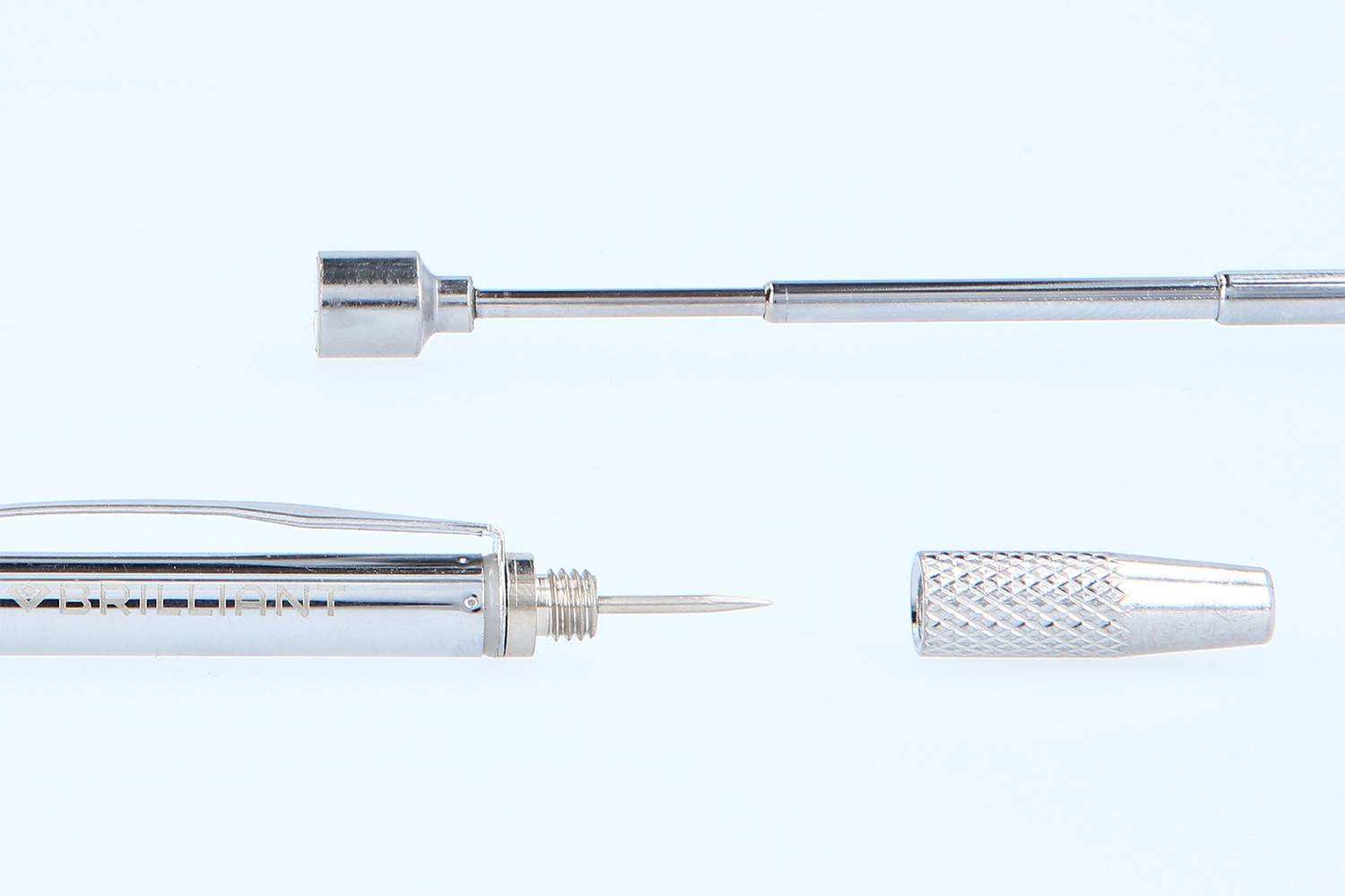 Zerlegter metallischer Stift, bestehend aus Spitze, Schaft und abnehmbarem Deckel, auf hellblauem Hintergrund.