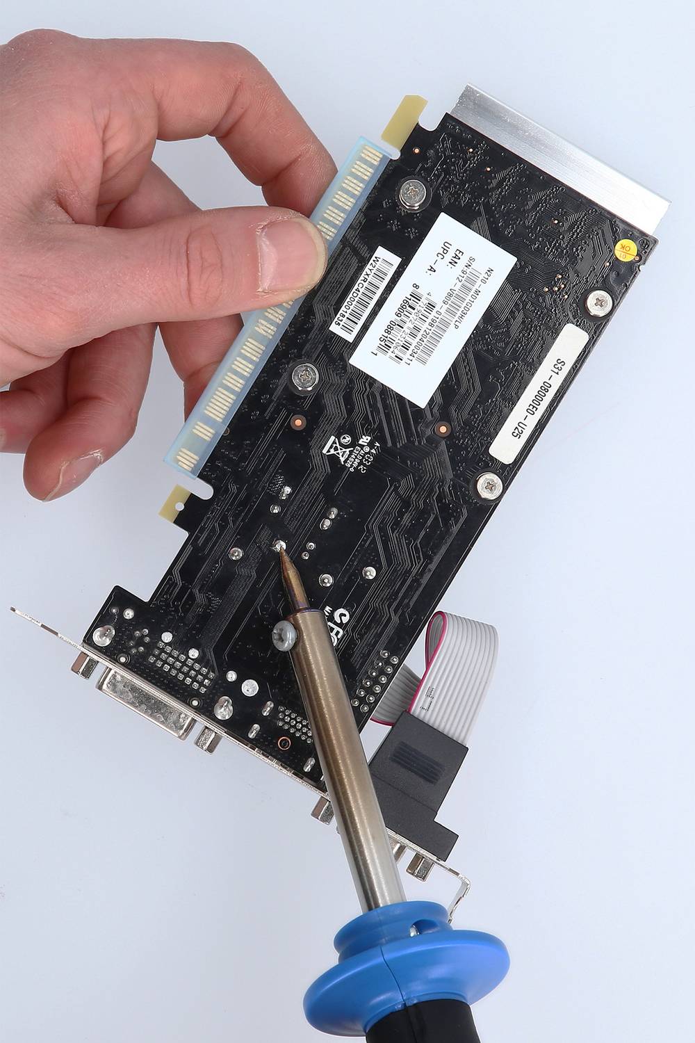 Eine Hand hält eine Grafikkarte, während ein Lötkolben die Rückseite berührt, vermutlich um Reparaturen oder Modifikationen vorzunehmen.