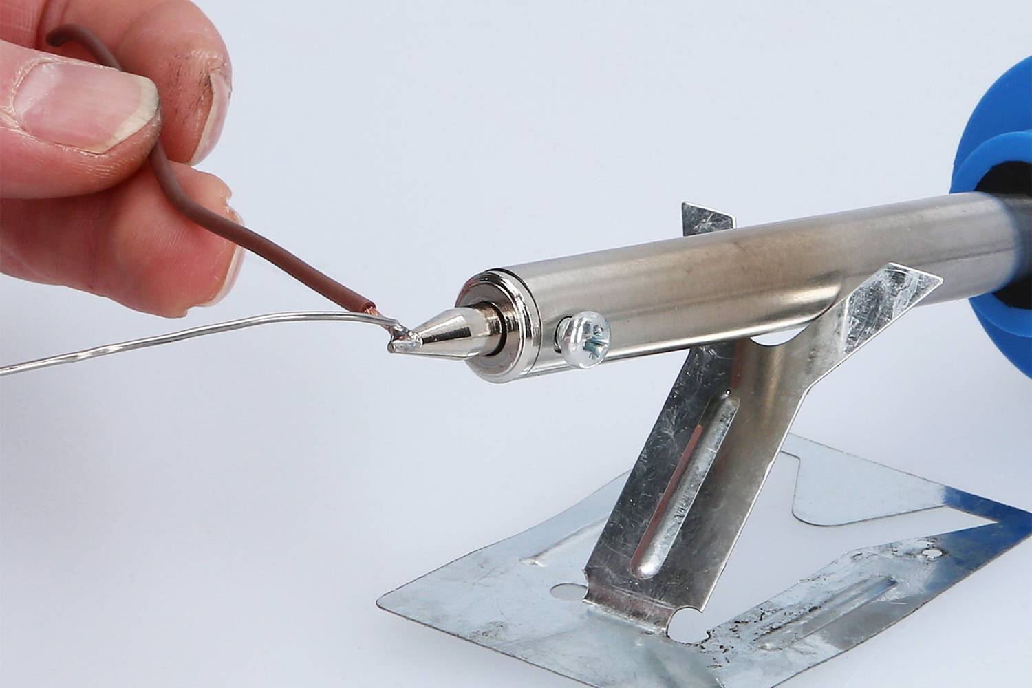 Eine Hand hält einen Draht nahe an eine Lötspitze eines Lötkolbens, die auf einem Metallständer ruht.