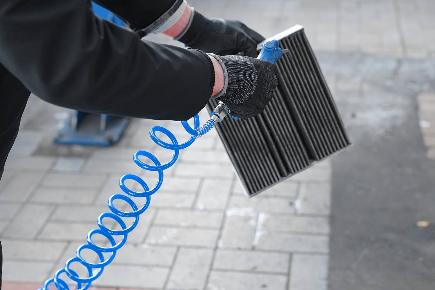 Eine Person reinigt mit einem blauen Druckluftschlauch einen Fahrzeugluftfilter, um Schmutz und Staub zu entfernen.