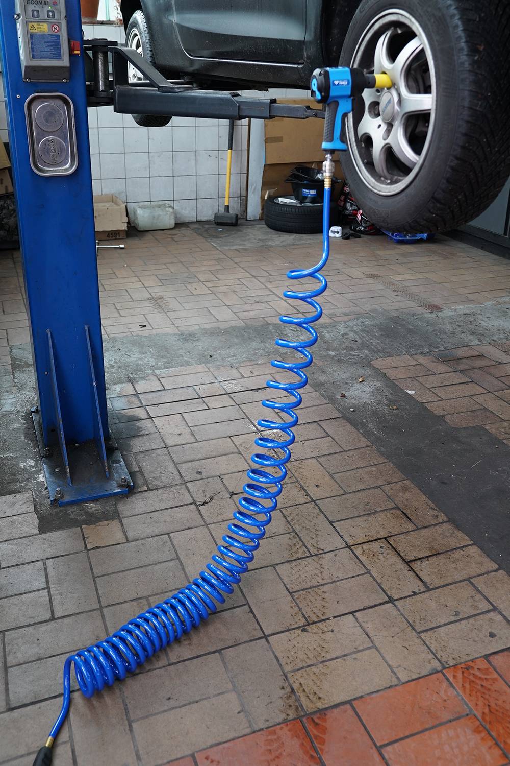 Auto auf Hebebühne mit Luftkompressor zum Reifenwechsel. Blaue Spiralschlauchleitung am Boden.