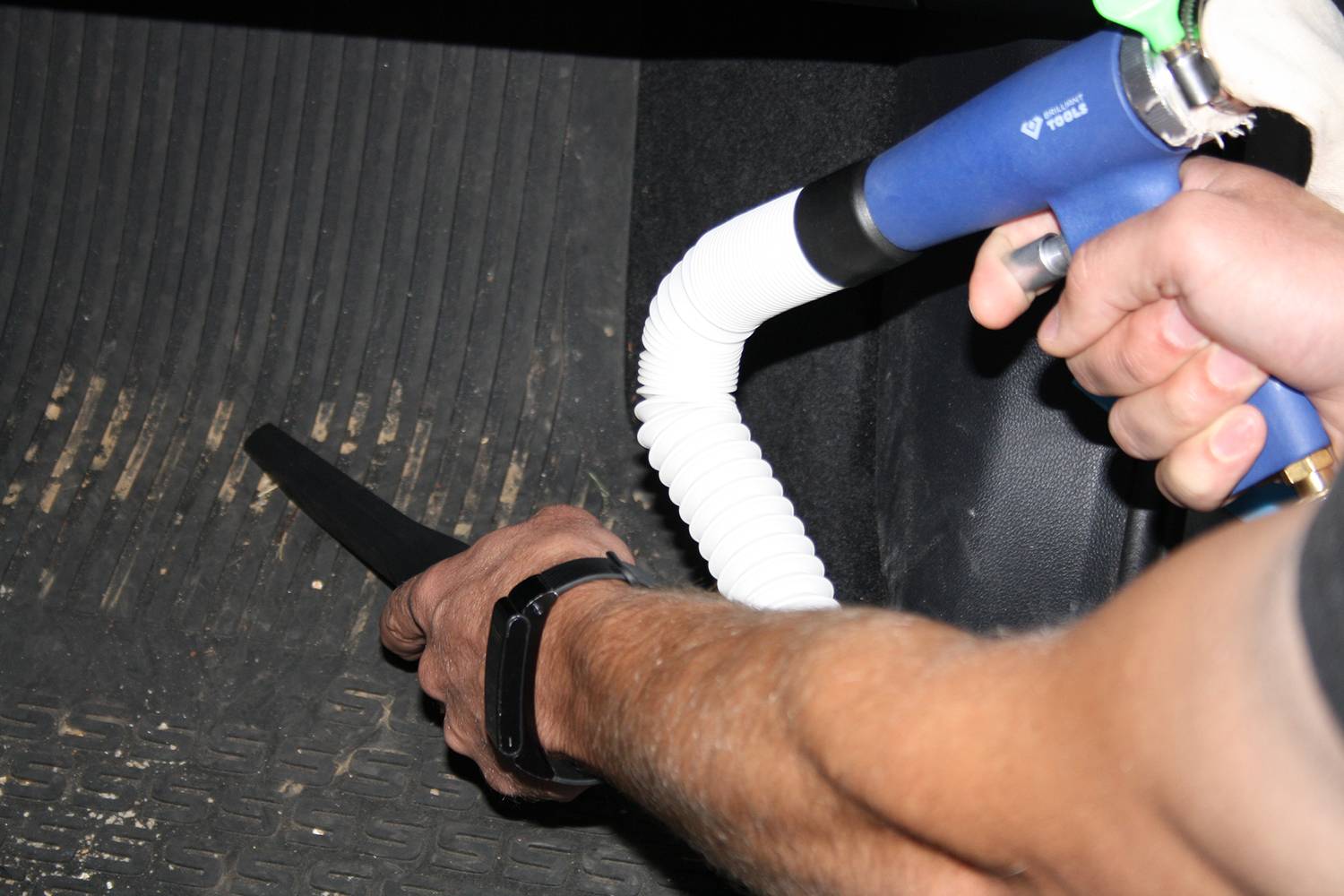 Ein Mann reinigt den Fußraum eines Autos mit einem blauen Staubsauger, der an einem weißen Schlauch befestigt ist.