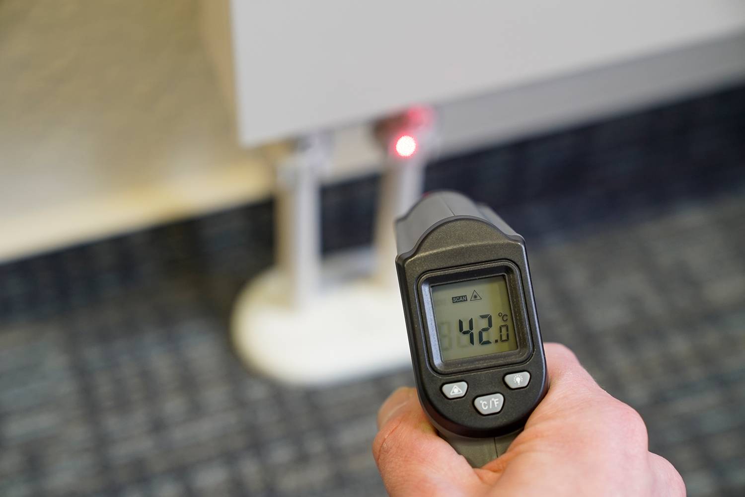 Person hält ein Infrarot-Thermometer vor einem Heizkörper, das 42,6 Grad Celsius anzeigt. температура отображающая на устройства момент измерения.