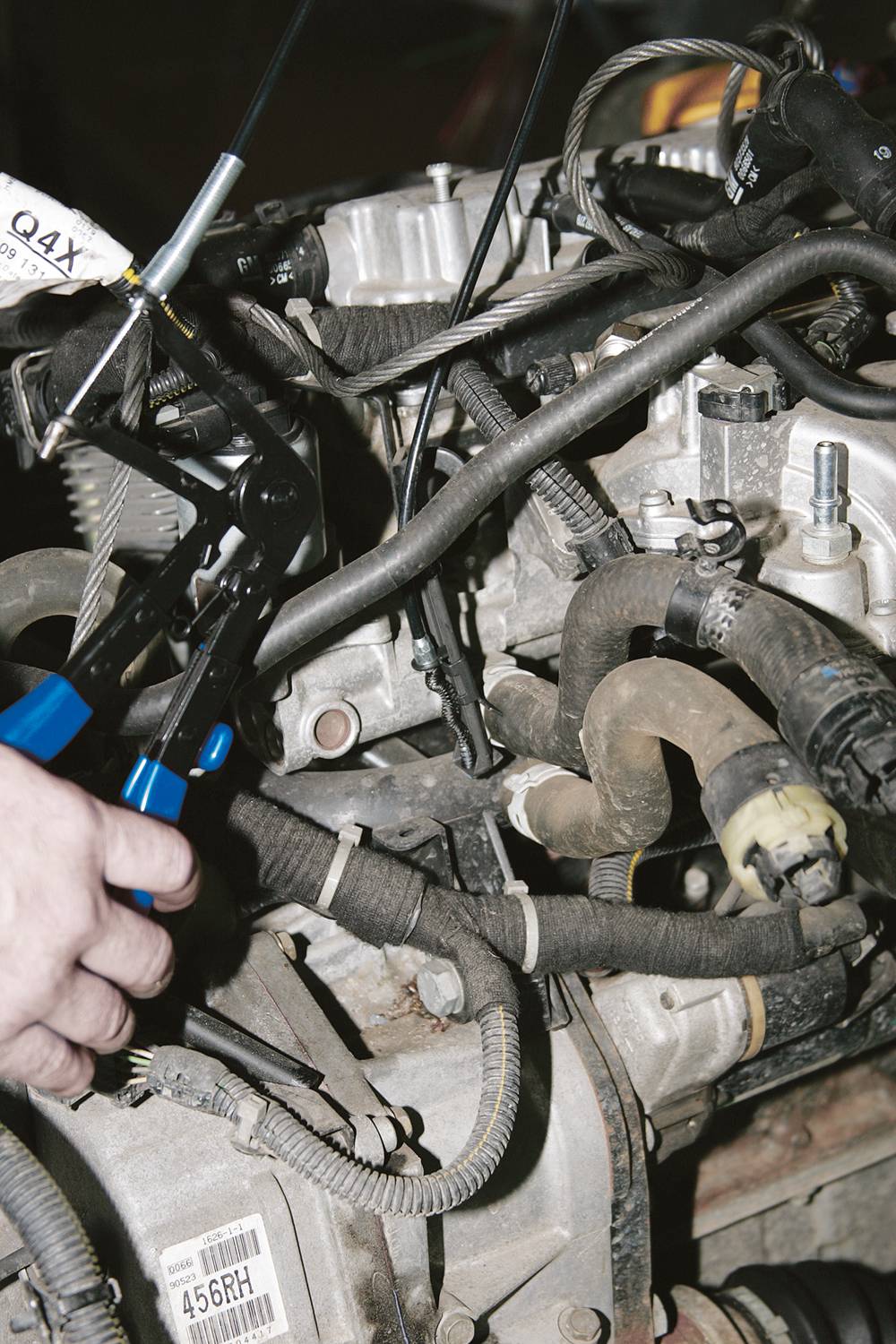 Motor mit sichtbaren Kabeln und Schläuchen, eine Hand hält Zange, scheint an Motorbauteilen zu arbeiten.